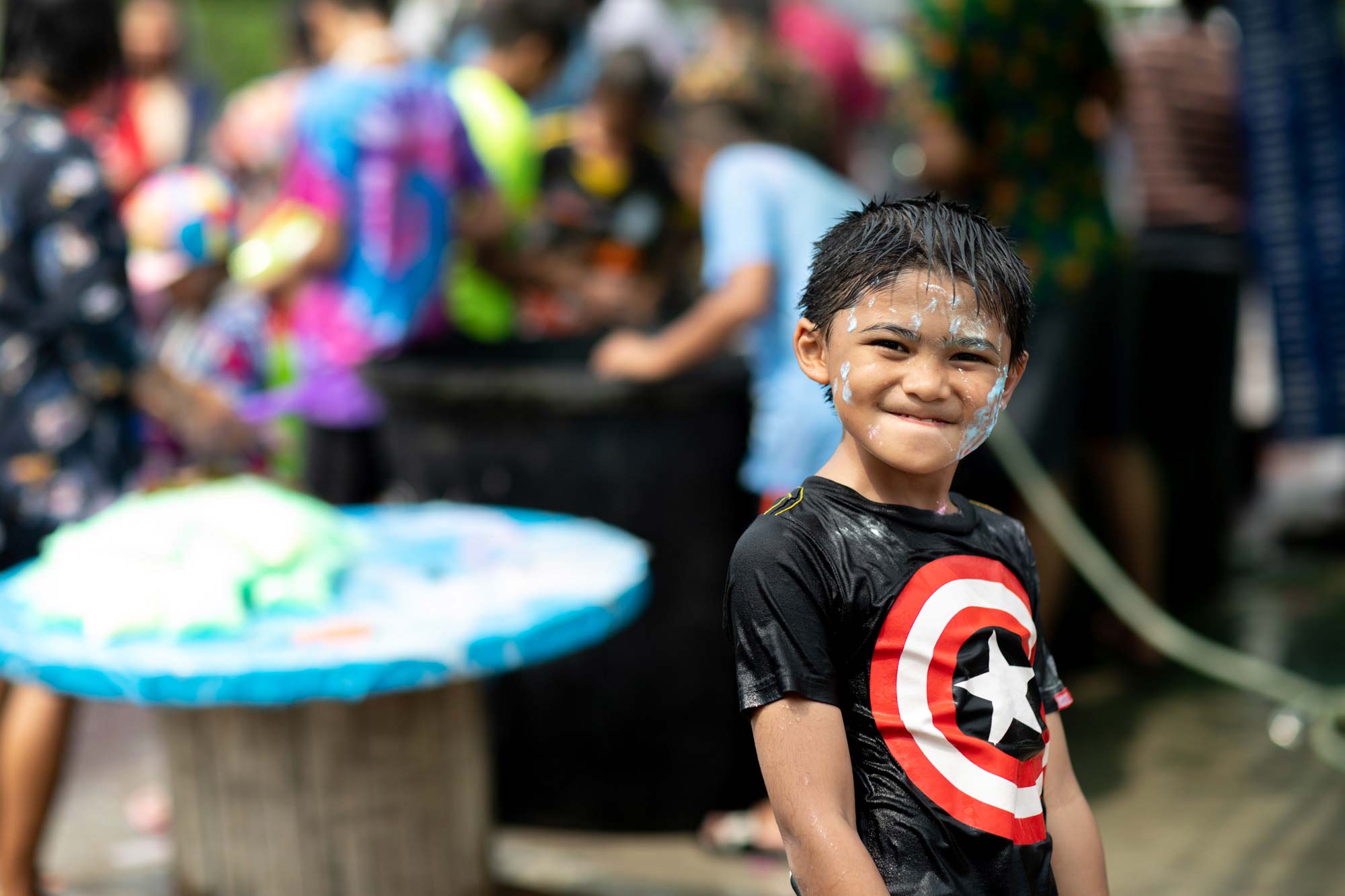 Portrait of a smiling Thai boy in a Captain America shirt with white Songkran powder smeared on his face during the water festival.