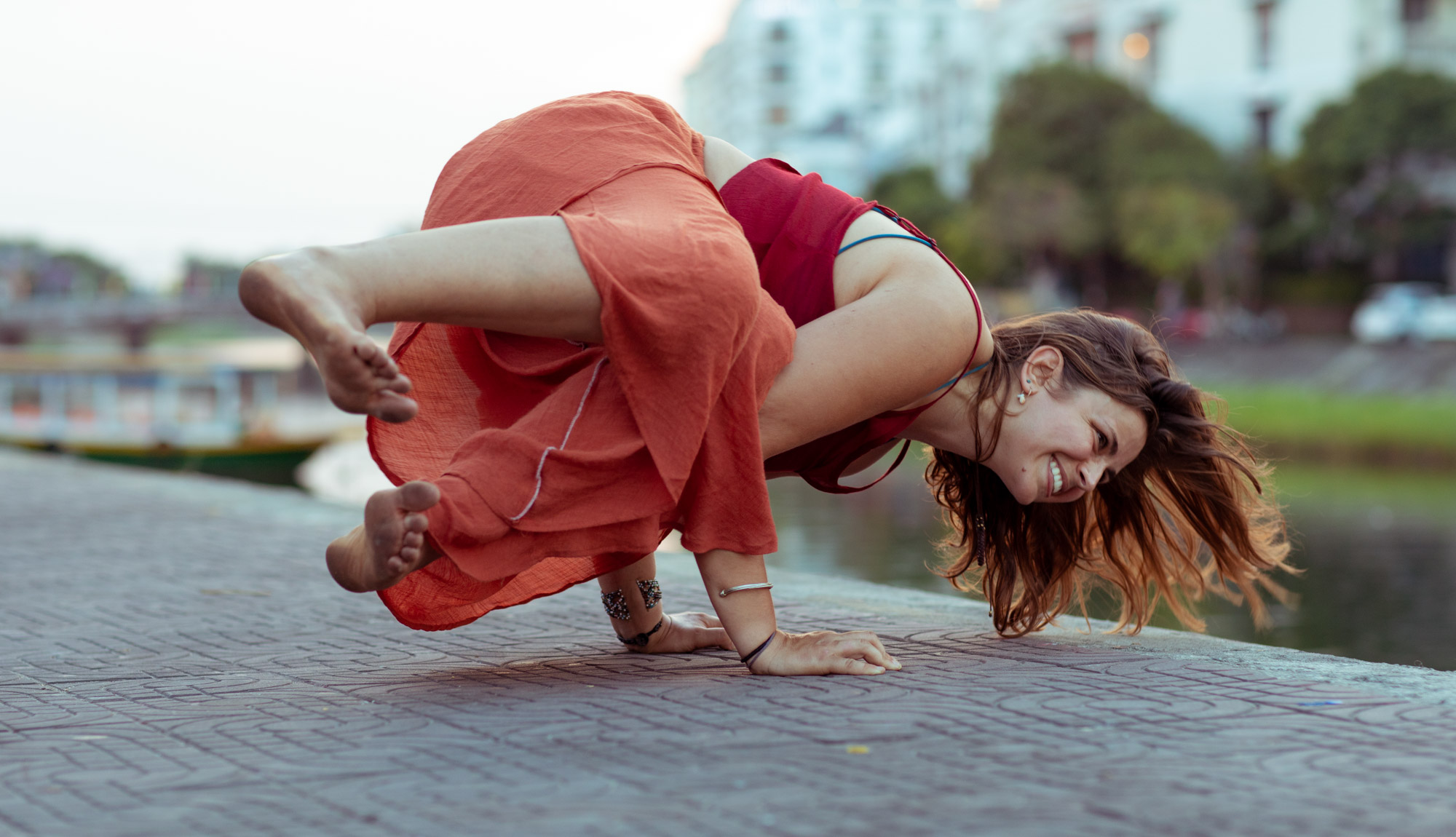 Emilia Semrau laughs through a crow arm-balance pose on a riverside walk in Hoi An, Vietnam.