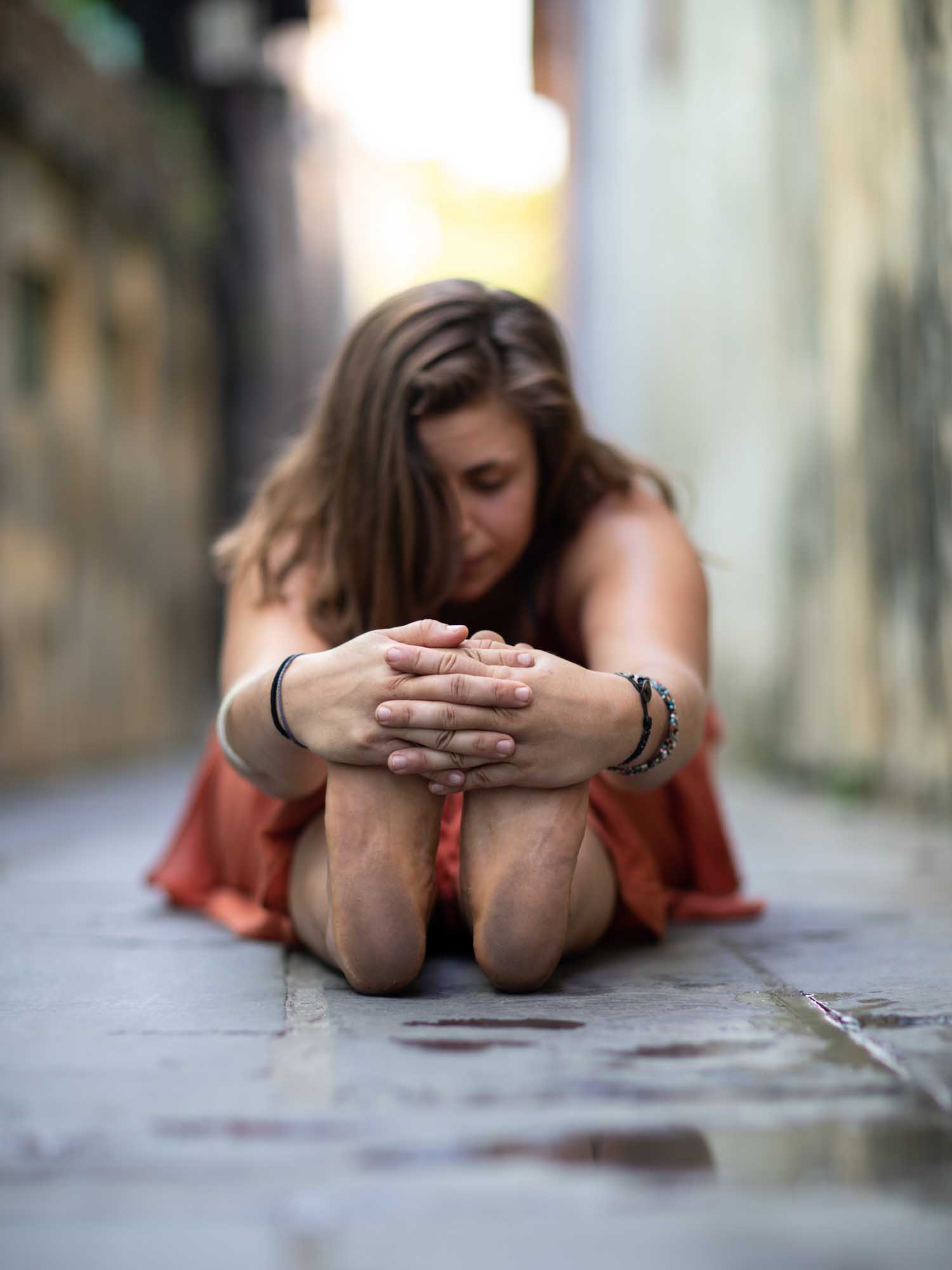 Emilia Semrau in a seated forward-fold yoga pose in a narrow, weathered alleyway in Hoi An, Vietnam.