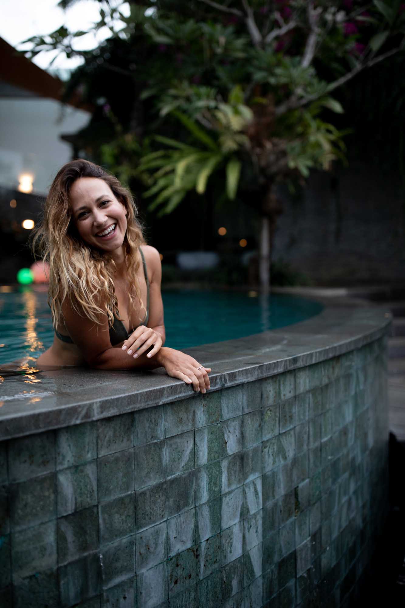 Blonde woman laughs at the edge of a slate-tiled infinity pool at dusk — Toraja Villa, Canggu, Bali.