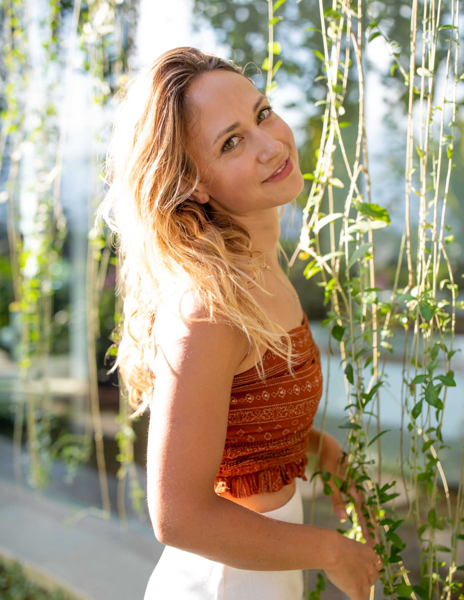 Golden-hour portrait of a blonde woman in a rust-orange smocked crop top among hanging vines at Toraja Villa, Canggu, Bali.