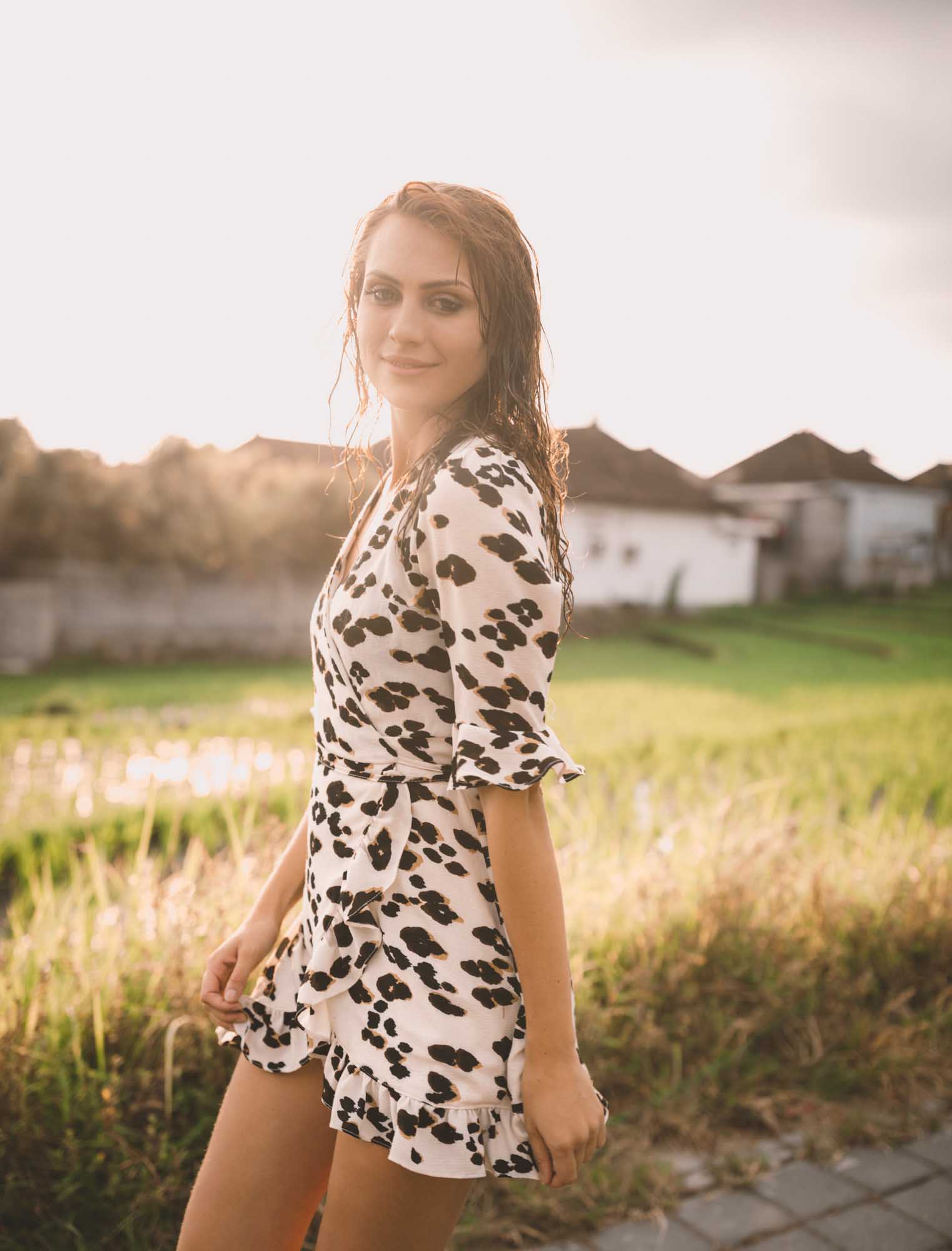 A redhead in a black-and-white spotted wrap dress walks a path at golden-hour beside a Canggu rice paddy, Bali.