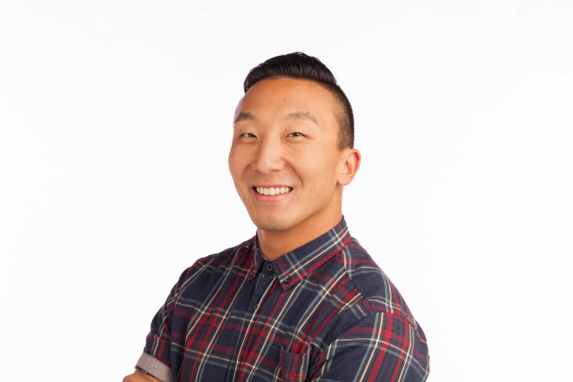 Studio headshot of Ben Song on a white background — black hair, arms crossed, wearing a navy-and-red tartan flannel button-down.