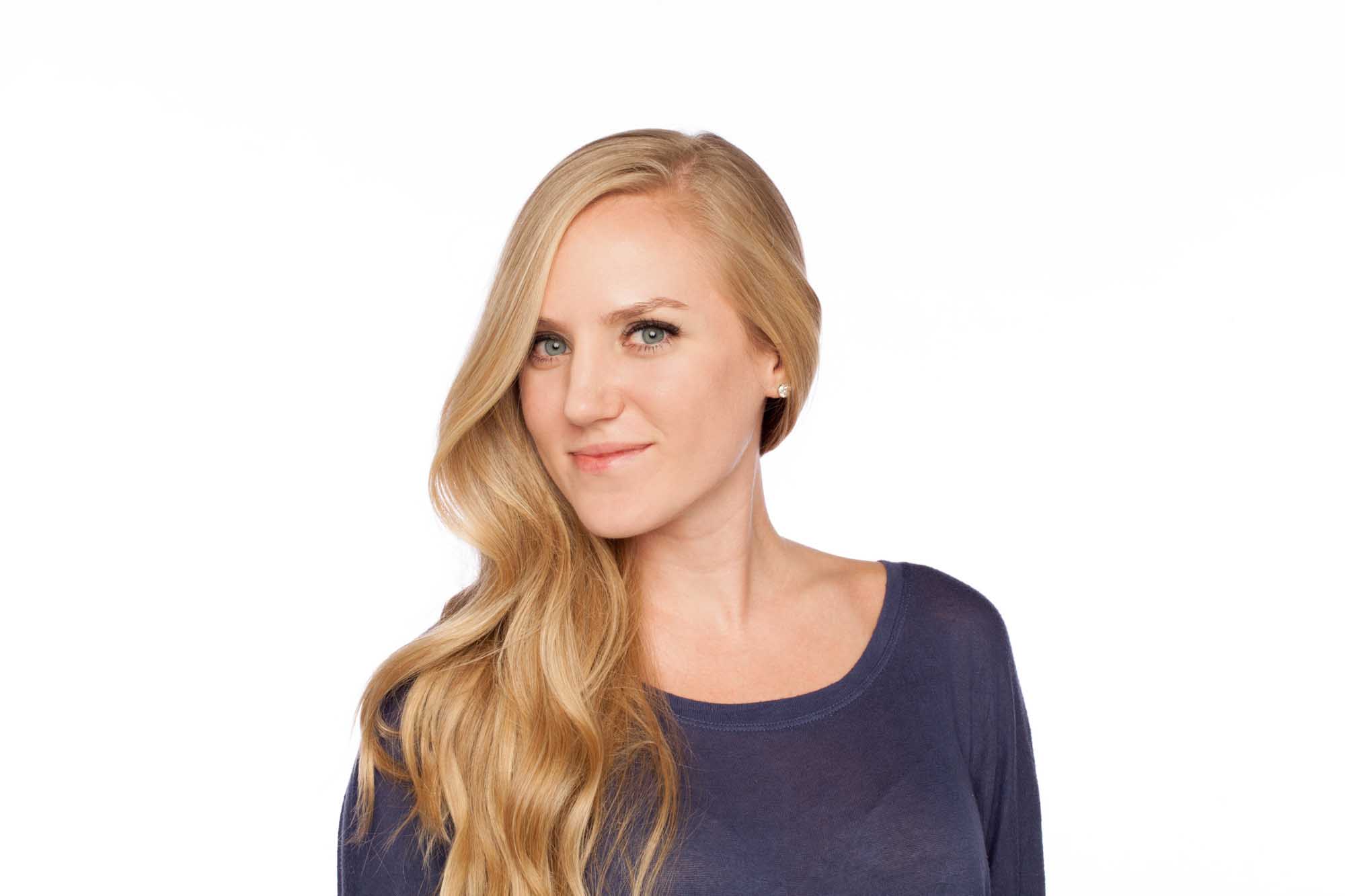 Studio headshot of Kendall Schultz on a white background — long blonde hair, navy long-sleeve top, subtle smile.