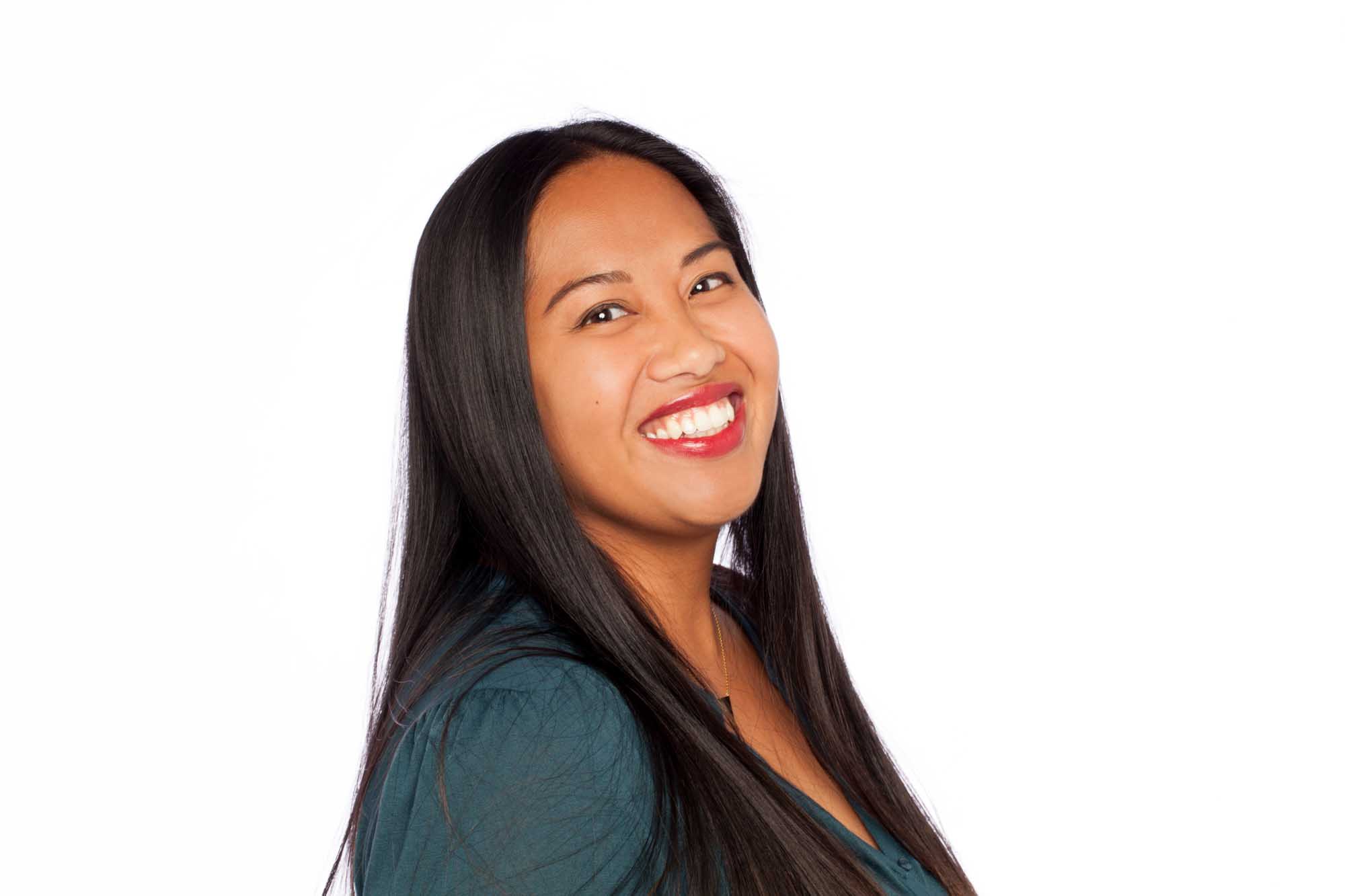 Studio headshot of Rosie Ollero on a white background — long dark hair, red lipstick, dark teal top, laughing with head tilted.