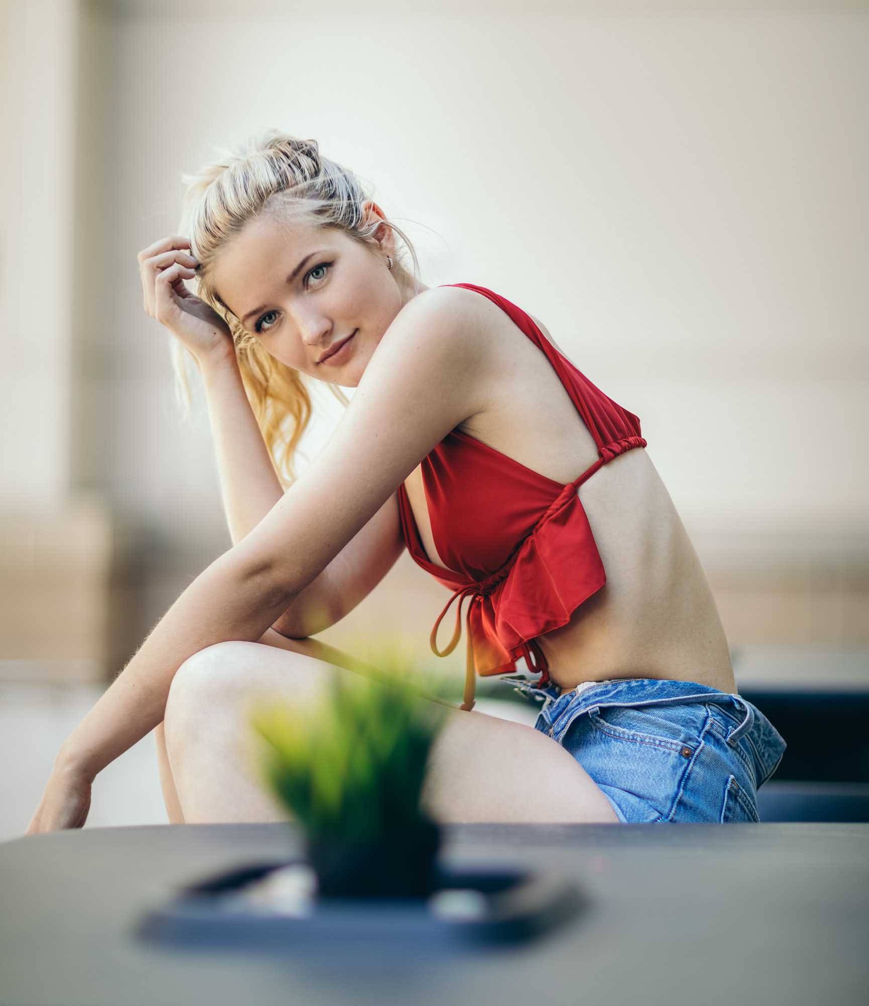Lifestyle portrait of Meghan Travers (@traversmeghan) in a red halter crop top and denim shorts sitting on a ledge in Denver, Colorado.