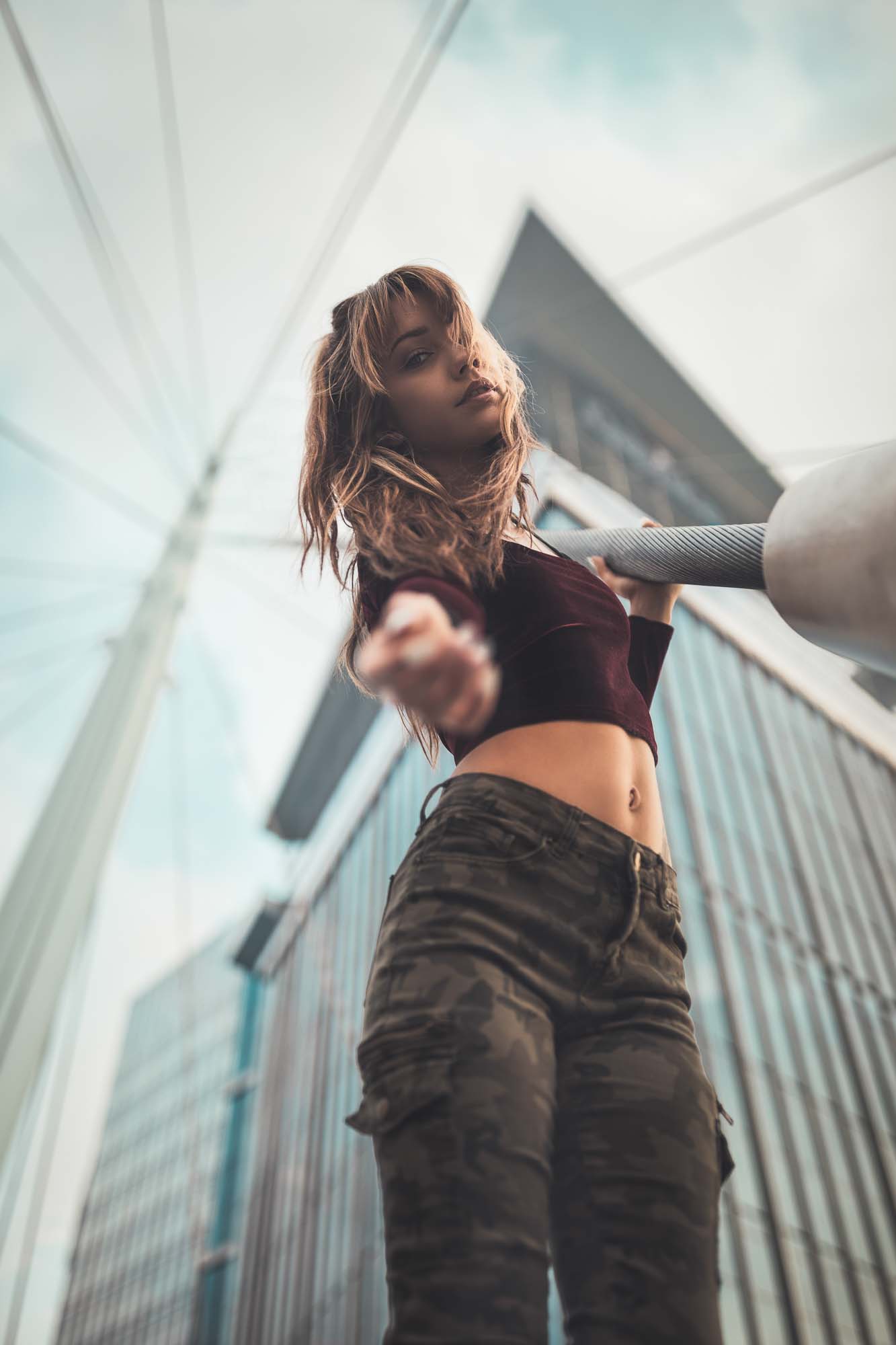 Low-angle Denver fashion shot of model @space.junkiee in camo pants in front of a downtown skyscraper