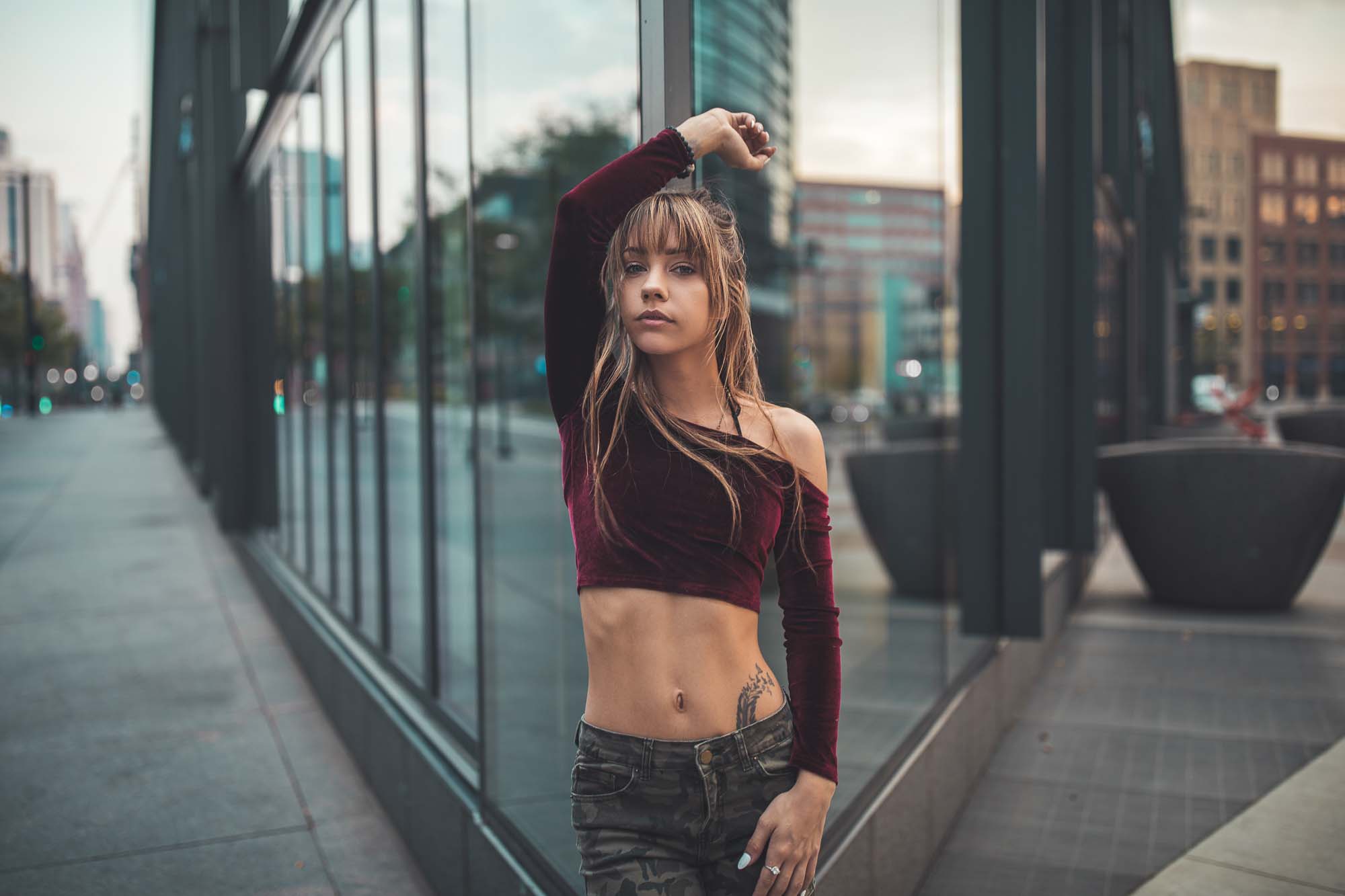 Street-style fashion photograph of model @space.junkiee in a burgundy crop top in front of a glass building in downtown Denver