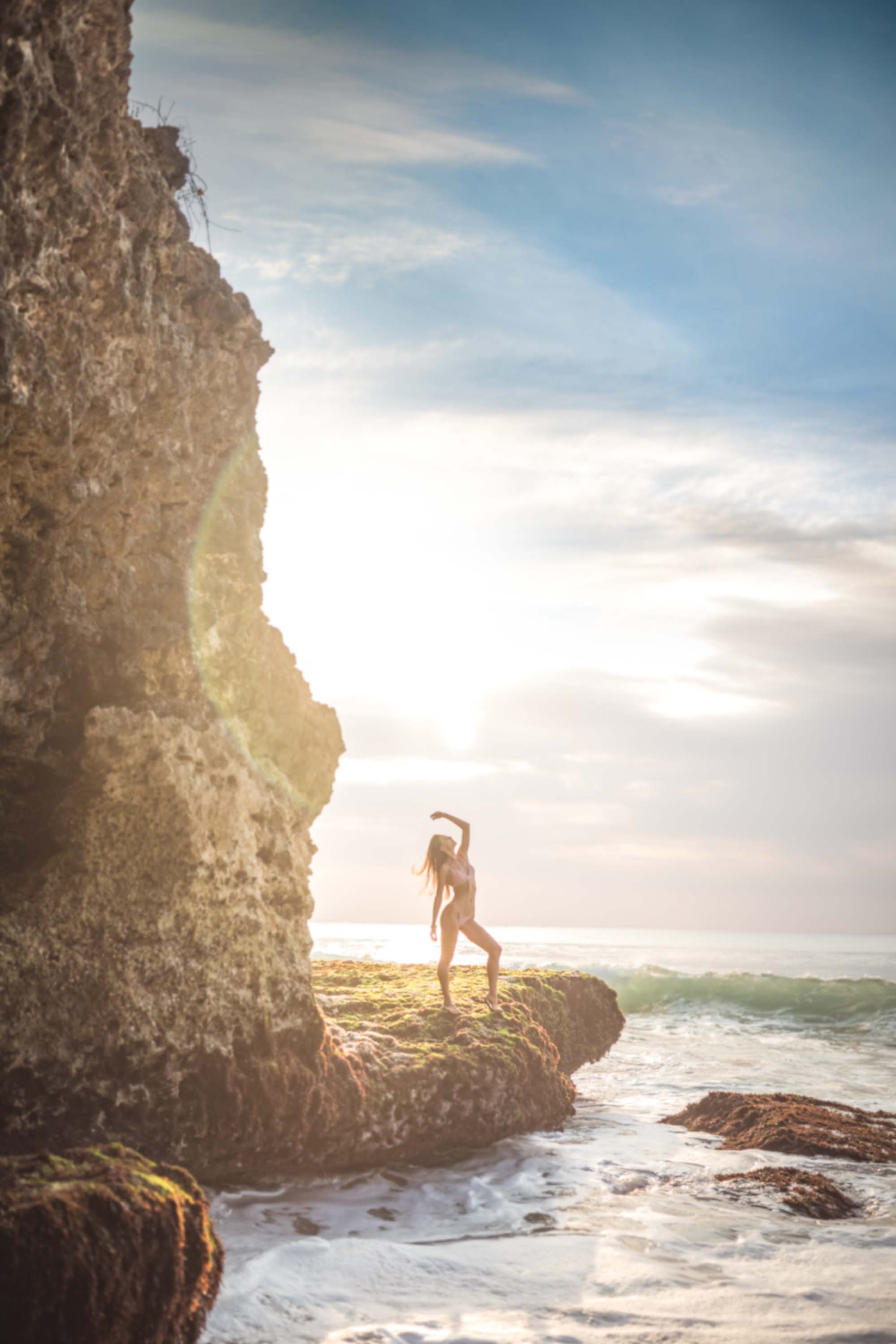 Fashion lifestyle portrait of a model standing on seaside rocks in Bali during golden hour
