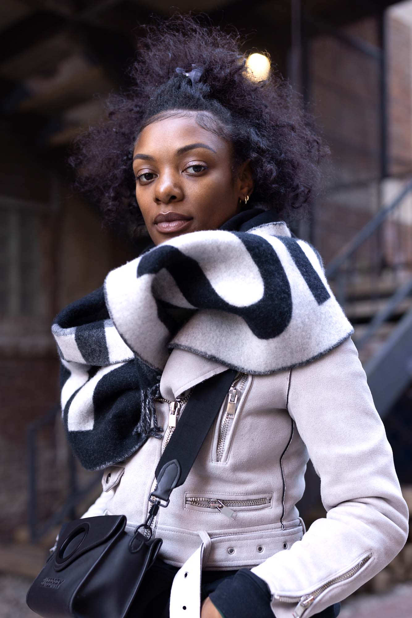 Close-up street-style portrait of a woman with a calm, composed expression in downtown Denver, wearing a cream leather jacket and a black-and-white patterned wool scarf.
