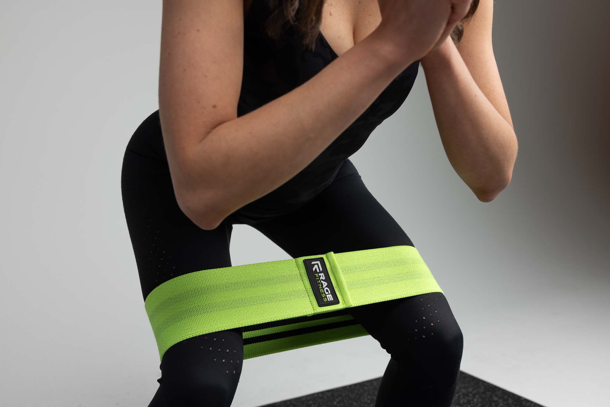 Female fitness model squatting with a Rage Fitness fabric hip resistance band, Denver studio lifestyle product shoot