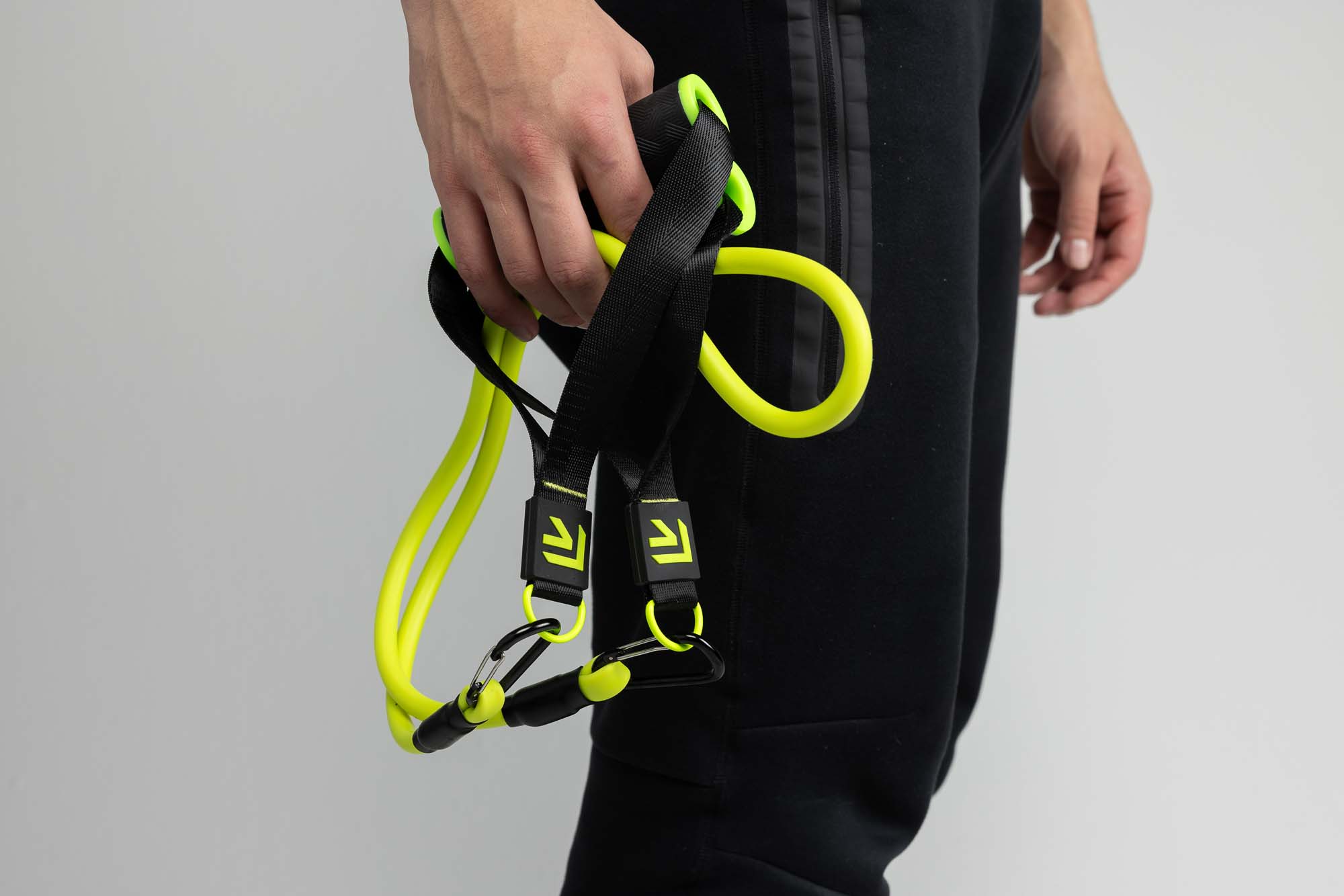 Close-up of an athlete gripping the foam handles of a Rage Fitness resistance-tube trainer set against a grey studio backdrop.