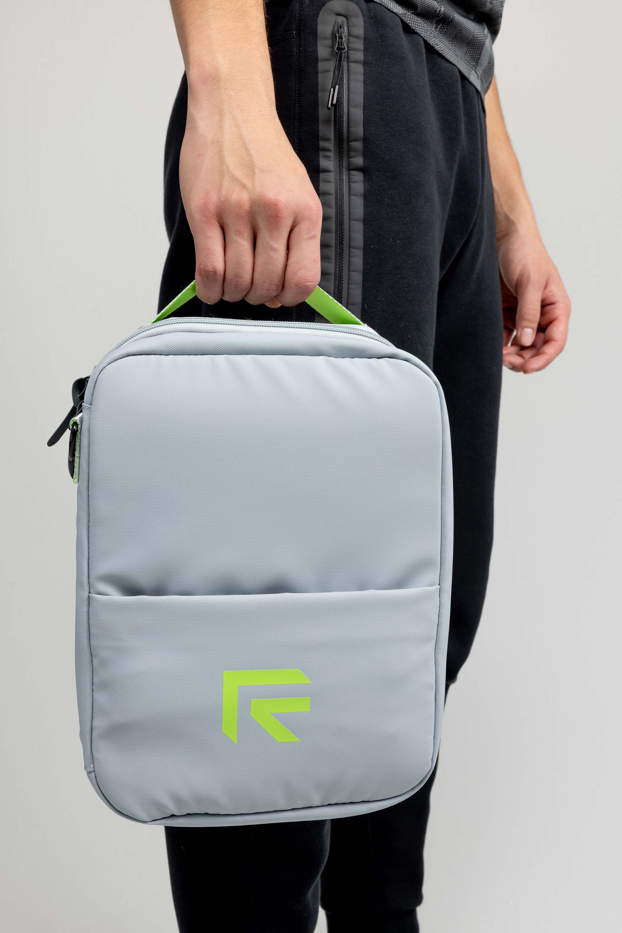 An athlete in black sweats carries a grey Rage Fitness gym accessory bag with neon-green branded logo and handle.