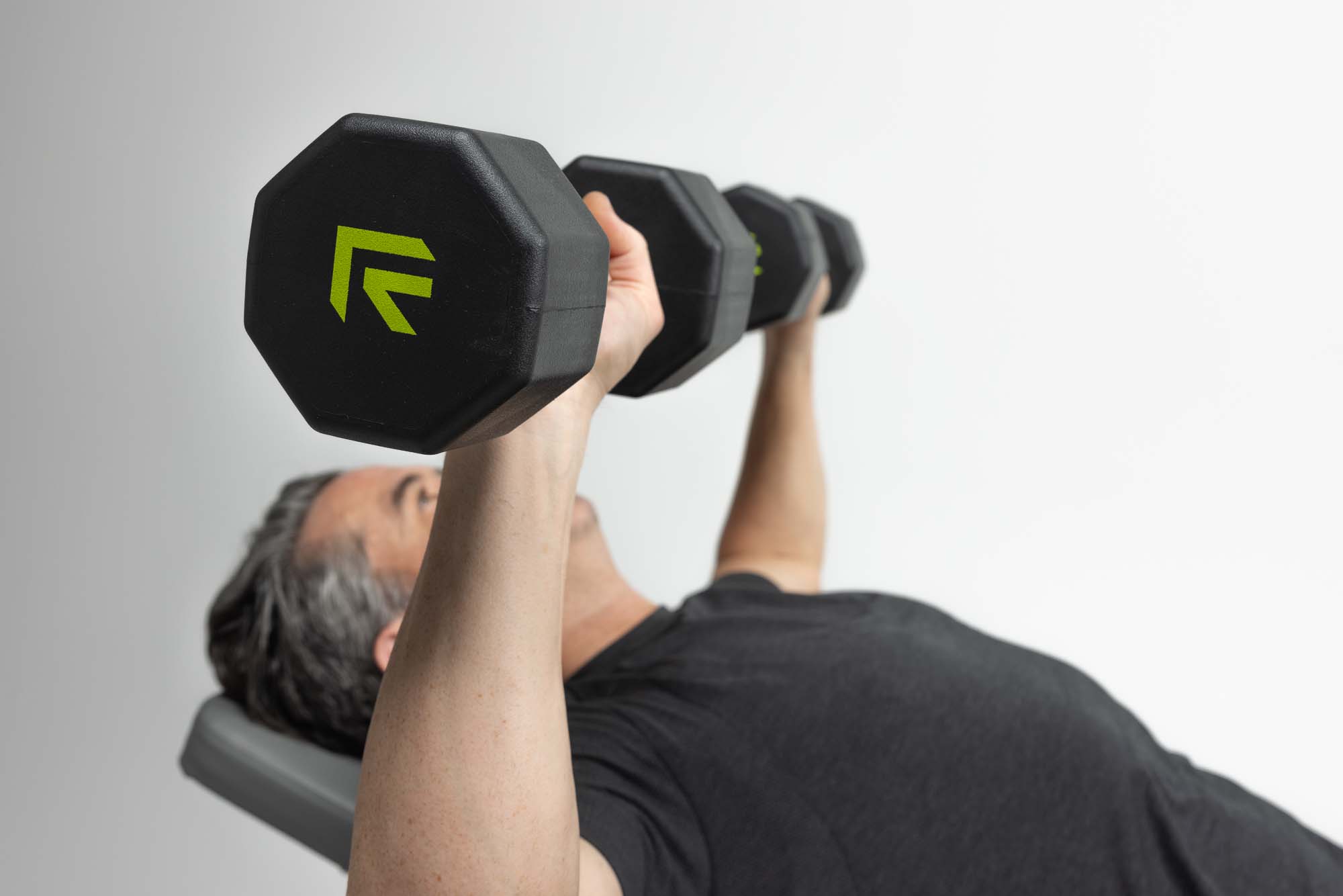 Bench press with a pair of black Rage Fitness hex dumbbells, neon green logo visible on the end caps