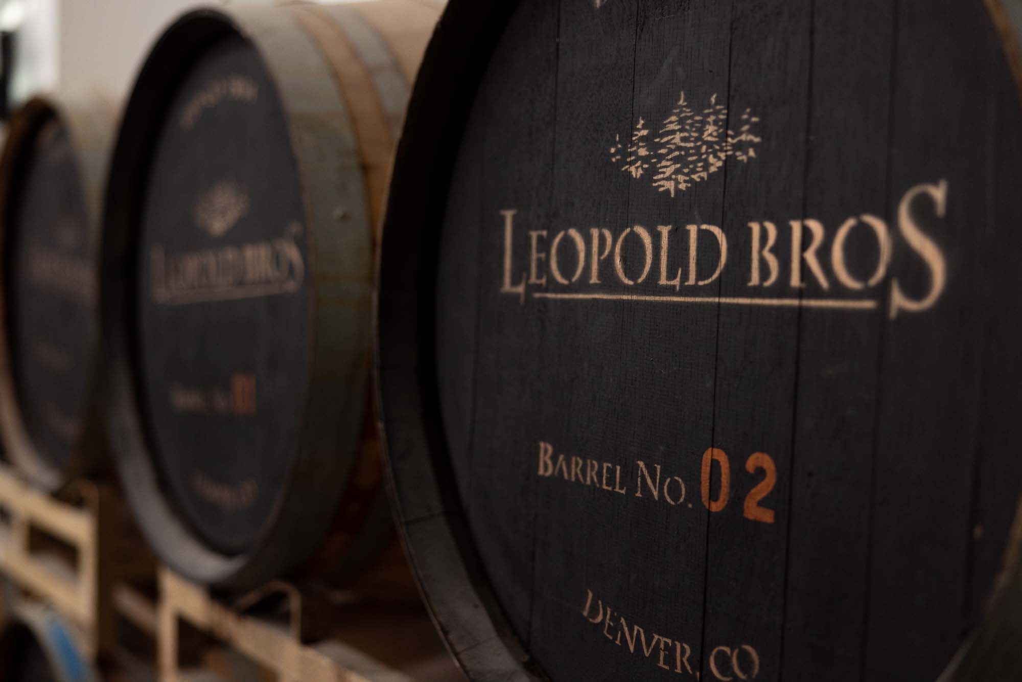 Close-up of a black Leopold Bros whiskey barrel branded "Barrel No. 02, Denver, CO" resting on a rack in the aging warehouse